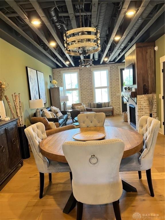 dining area featuring a fireplace, a notable chandelier, brick wall, and light hardwood / wood-style flooring