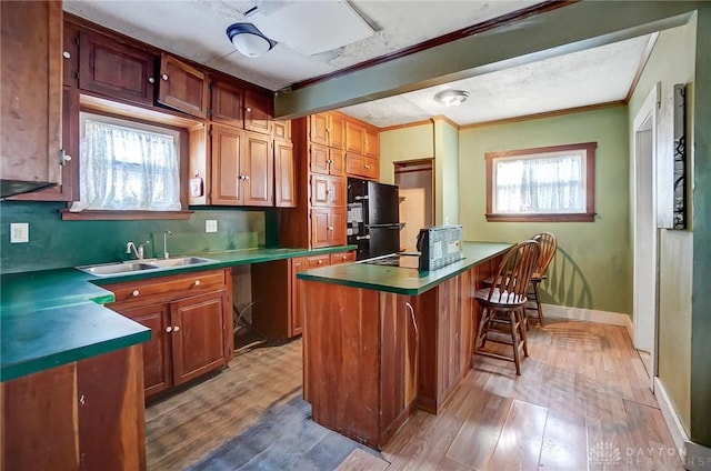 kitchen featuring a kitchen island, wood-type flooring, sink, black fridge, and ornamental molding