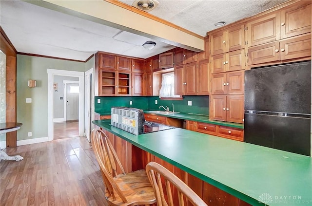 kitchen featuring a textured ceiling, sink, black fridge, ornamental molding, and light hardwood / wood-style flooring