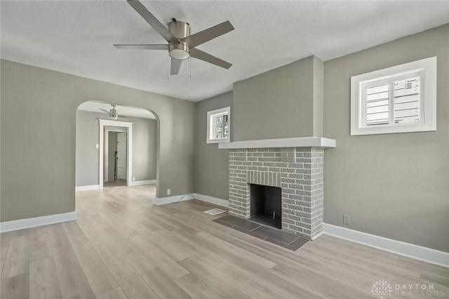 unfurnished living room featuring a textured ceiling, ceiling fan, a wealth of natural light, and a brick fireplace