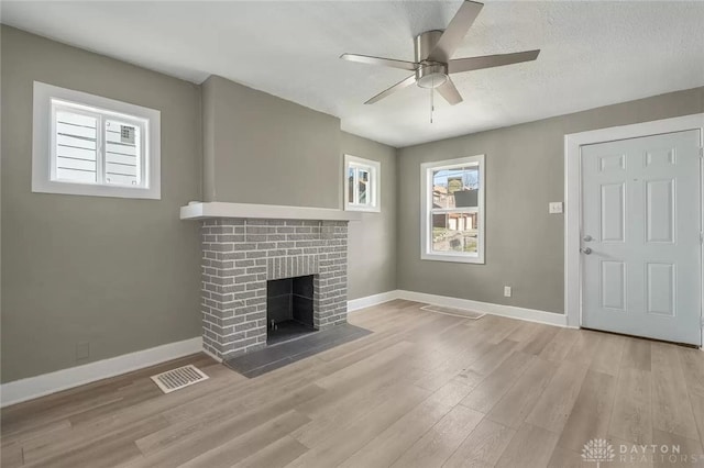 unfurnished living room with ceiling fan, light wood-type flooring, a brick fireplace, and a textured ceiling