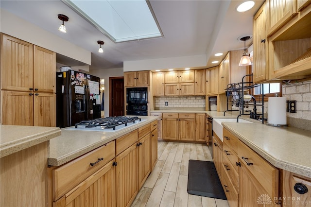 kitchen featuring a skylight, backsplash, hanging light fixtures, light hardwood / wood-style flooring, and black appliances