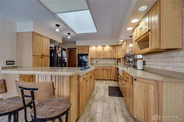 kitchen with a skylight, light hardwood / wood-style floors, decorative backsplash, light brown cabinets, and black appliances