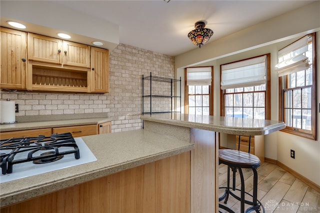 kitchen featuring backsplash, a breakfast bar, white gas cooktop, and light brown cabinets