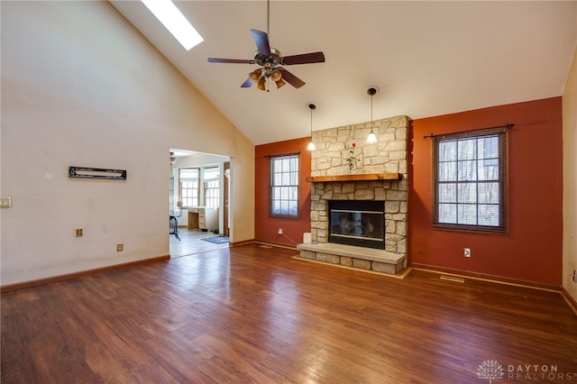 unfurnished living room featuring ceiling fan, a skylight, dark wood-type flooring, a stone fireplace, and high vaulted ceiling