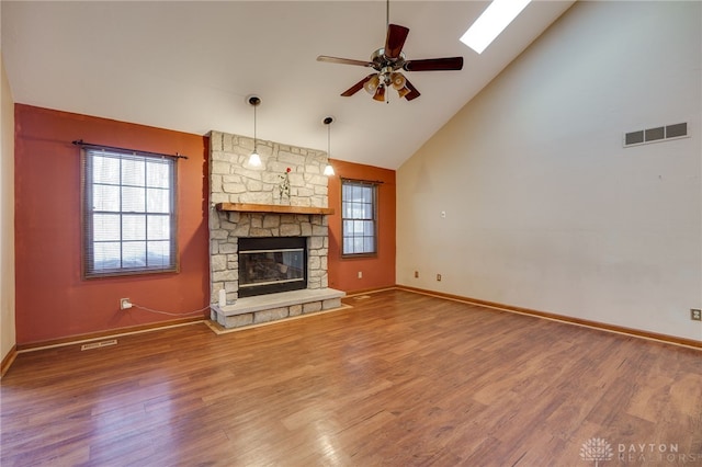 unfurnished living room featuring ceiling fan, a fireplace, wood-type flooring, a skylight, and high vaulted ceiling