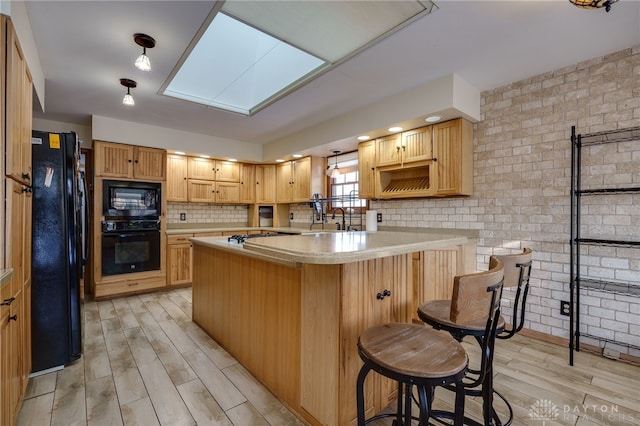 kitchen featuring a skylight, sink, a breakfast bar, and black appliances