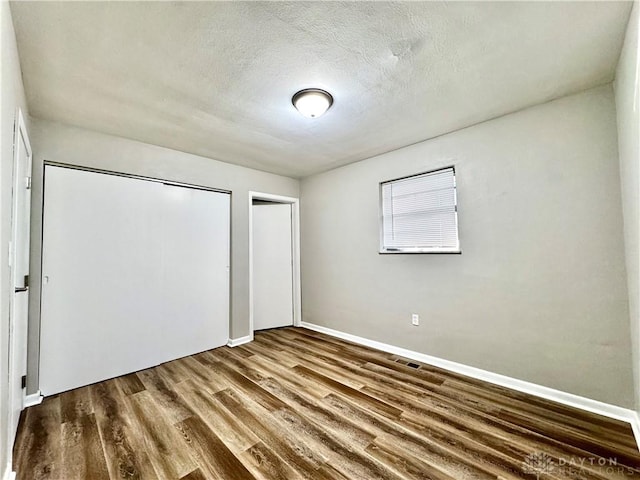 unfurnished bedroom featuring visible vents, a textured ceiling, baseboards, and wood finished floors