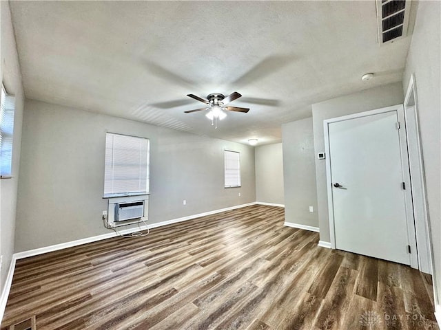 empty room with a wall mounted air conditioner, visible vents, baseboards, and wood finished floors