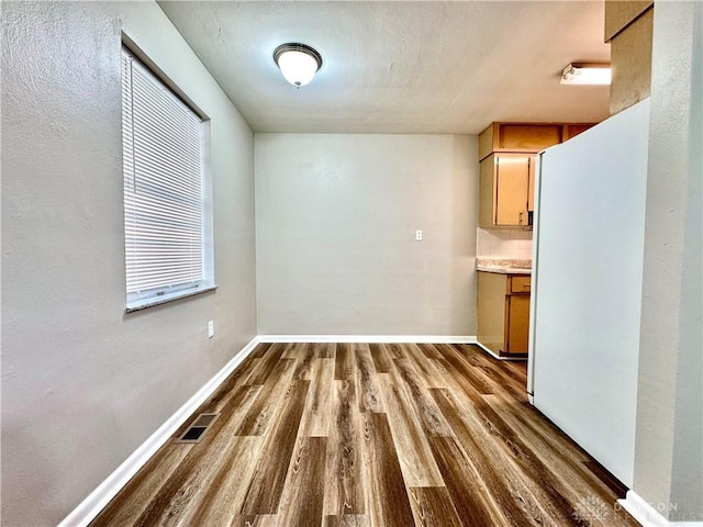 unfurnished dining area featuring dark wood-type flooring, visible vents, and baseboards