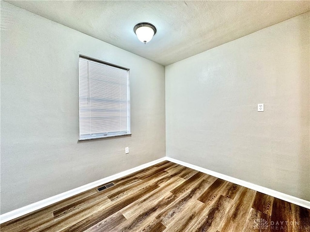 spare room with wood finished floors, visible vents, and baseboards