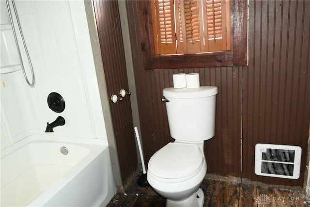 bathroom featuring toilet, bathing tub / shower combination, and wooden walls