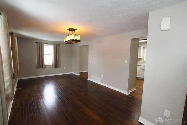 spare room featuring dark wood-type flooring, a chandelier, and a textured ceiling