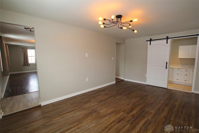 interior space with dark wood-type flooring, ensuite bathroom, a barn door, and a notable chandelier