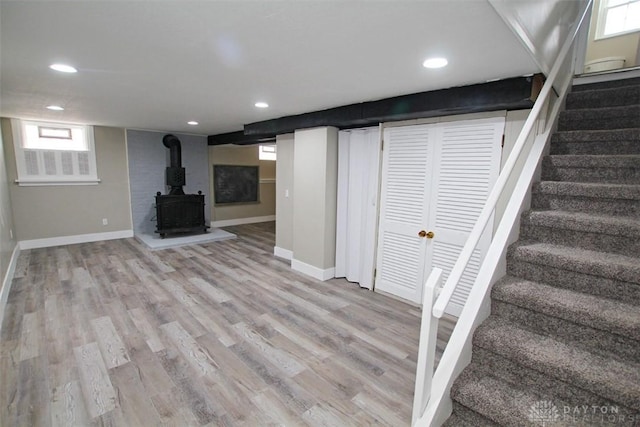 basement with a wood stove and light hardwood / wood-style flooring