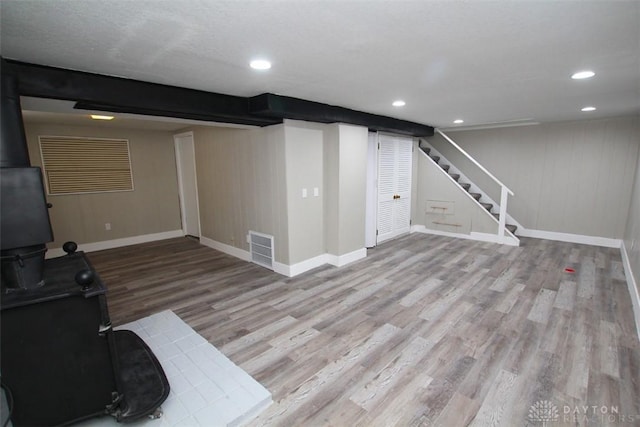 basement with a wood stove and light hardwood / wood-style flooring