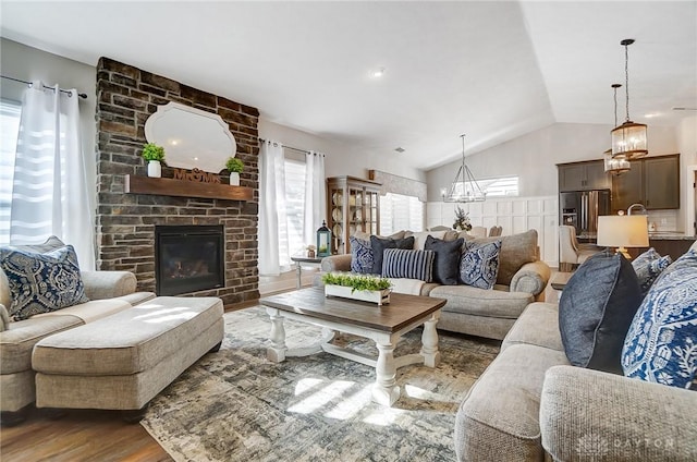 living room with vaulted ceiling, an inviting chandelier, a stone fireplace, and dark wood-type flooring