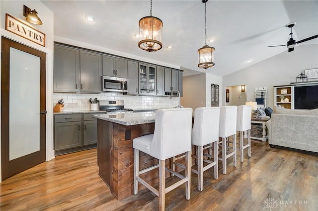 kitchen with stainless steel appliances, decorative backsplash, hanging light fixtures, a kitchen island with sink, and light stone counters