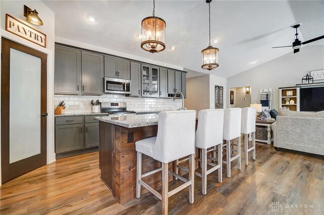 kitchen with stainless steel appliances, pendant lighting, a center island with sink, and light stone countertops