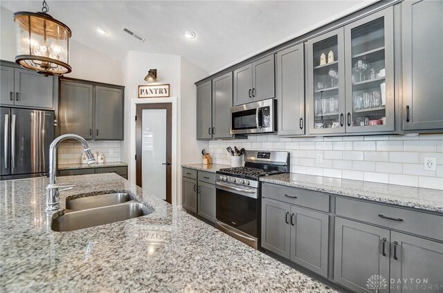 kitchen with backsplash, light wood-type flooring, light stone countertops, gray cabinetry, and stainless steel appliances