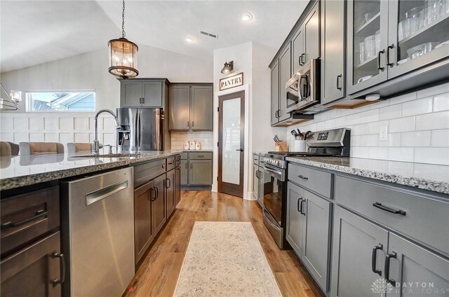 kitchen featuring a center island with sink, stainless steel appliances, backsplash, lofted ceiling, and sink