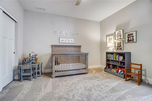 carpeted bedroom with ceiling fan, a closet, and a crib