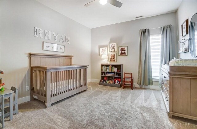 bedroom featuring ceiling fan, light colored carpet, a nursery area, ensuite bathroom, and a closet