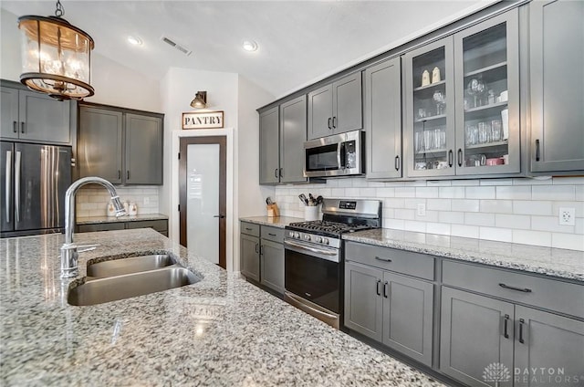 kitchen featuring light stone counters, sink, decorative light fixtures, and stainless steel appliances