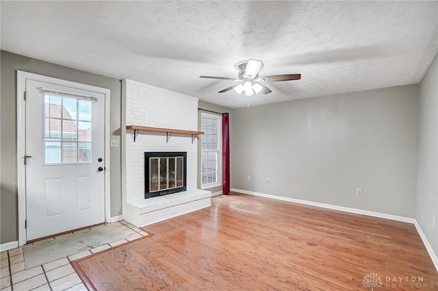 unfurnished living room featuring ceiling fan, a textured ceiling, light tile patterned floors, and a fireplace