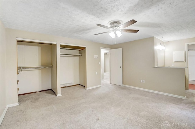 unfurnished bedroom featuring ceiling fan, two closets, light colored carpet, and a textured ceiling