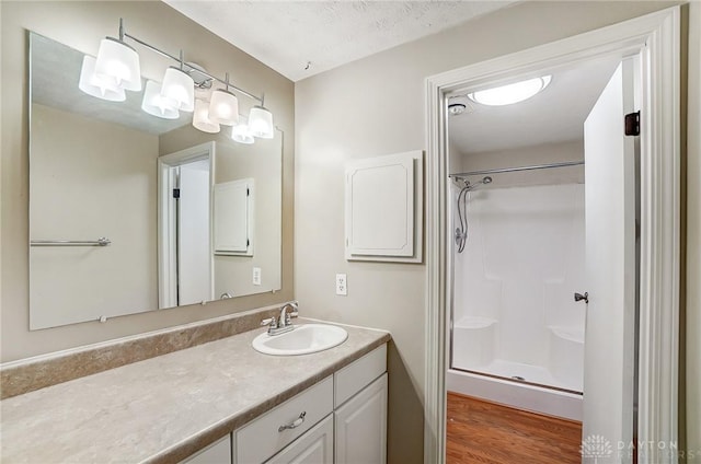 bathroom featuring a textured ceiling, hardwood / wood-style floors, walk in shower, and vanity