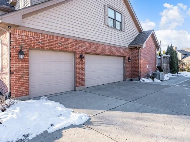 view of snowy exterior featuring central AC unit and a garage