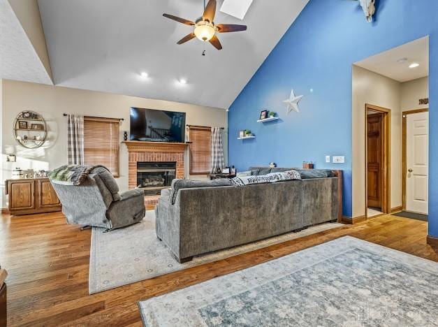 living room with high vaulted ceiling, ceiling fan, a brick fireplace, and hardwood / wood-style floors