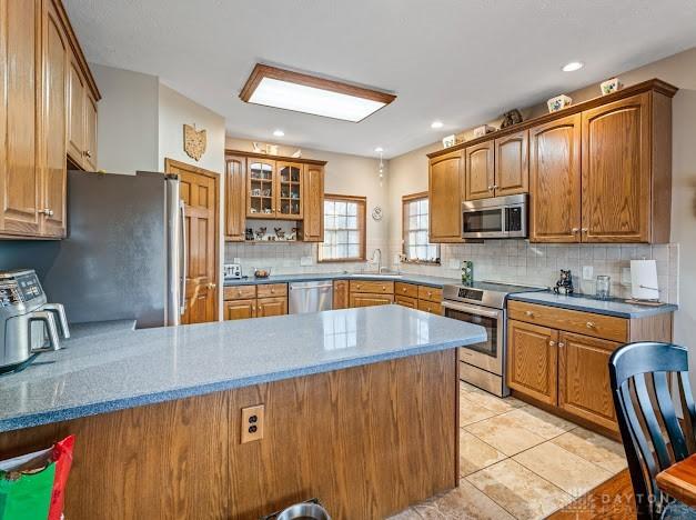 kitchen featuring kitchen peninsula, stainless steel appliances, backsplash, light tile patterned flooring, and sink