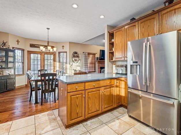 kitchen with light tile patterned floors, kitchen peninsula, stainless steel fridge with ice dispenser, and pendant lighting