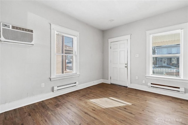 empty room with a wall mounted air conditioner, wood-type flooring, and a baseboard radiator