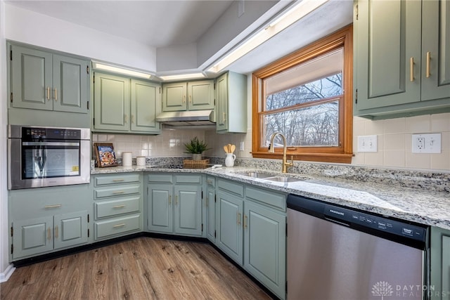 kitchen with wood-type flooring, stainless steel appliances, sink, light stone counters, and green cabinets