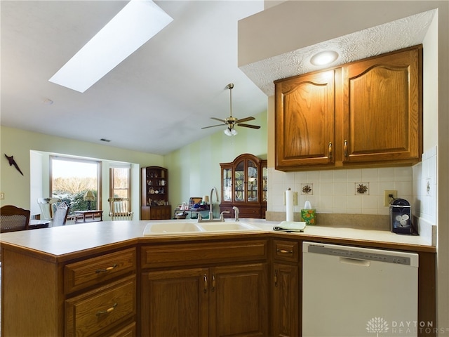 kitchen with vaulted ceiling with skylight, decorative backsplash, sink, kitchen peninsula, and white dishwasher