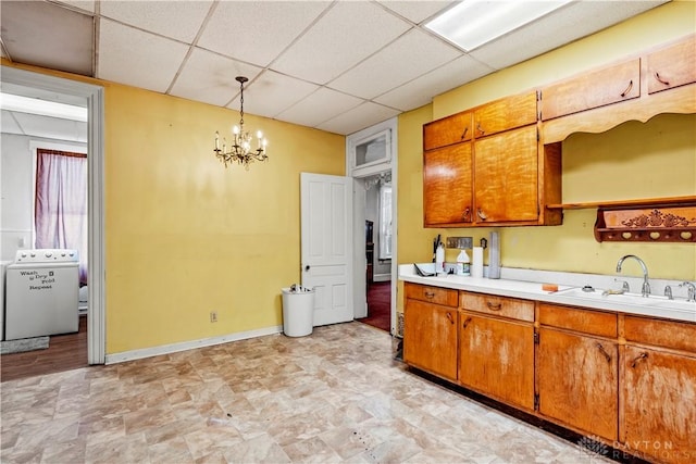 kitchen with a paneled ceiling, washer / clothes dryer, sink, hanging light fixtures, and a notable chandelier