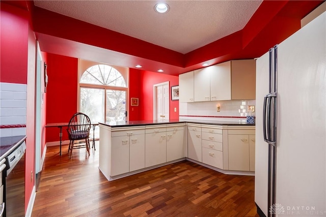 kitchen with dishwasher, white fridge, kitchen peninsula, white cabinets, and dark hardwood / wood-style flooring