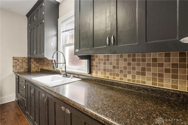 kitchen featuring dark wood-type flooring, sink, backsplash, and dark brown cabinets