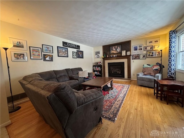 living room featuring a brick fireplace, a textured ceiling, and light hardwood / wood-style floors