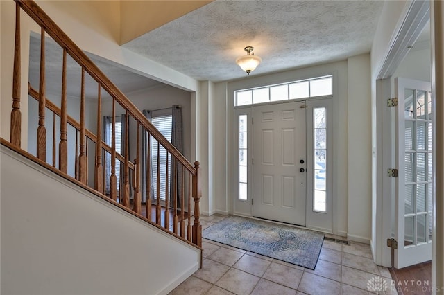 entrance foyer featuring baseboards, stairway, a textured ceiling, and light tile patterned floors