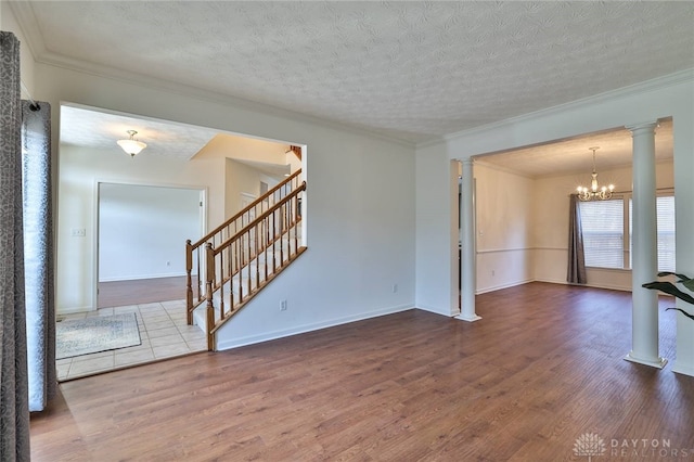 empty room featuring crown molding, stairs, decorative columns, and wood finished floors