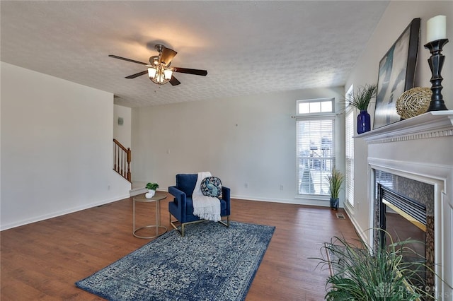 living area featuring stairway, dark wood finished floors, a textured ceiling, and a glass covered fireplace