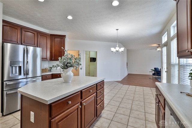 kitchen featuring light tile patterned floors, a kitchen island, light countertops, stainless steel fridge, and decorative light fixtures