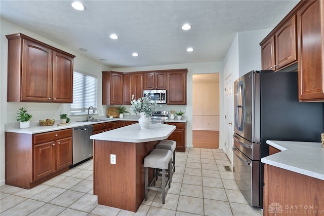 kitchen featuring stainless steel appliances, a sink, a kitchen island, a kitchen breakfast bar, and light countertops