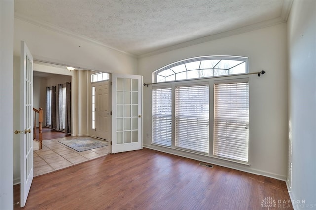 foyer entrance with crown molding, a textured ceiling, visible vents, and light wood-style floors