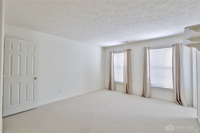 unfurnished room featuring light colored carpet, a textured ceiling, and baseboards