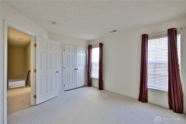 unfurnished bedroom with a closet, light carpet, visible vents, and a textured ceiling